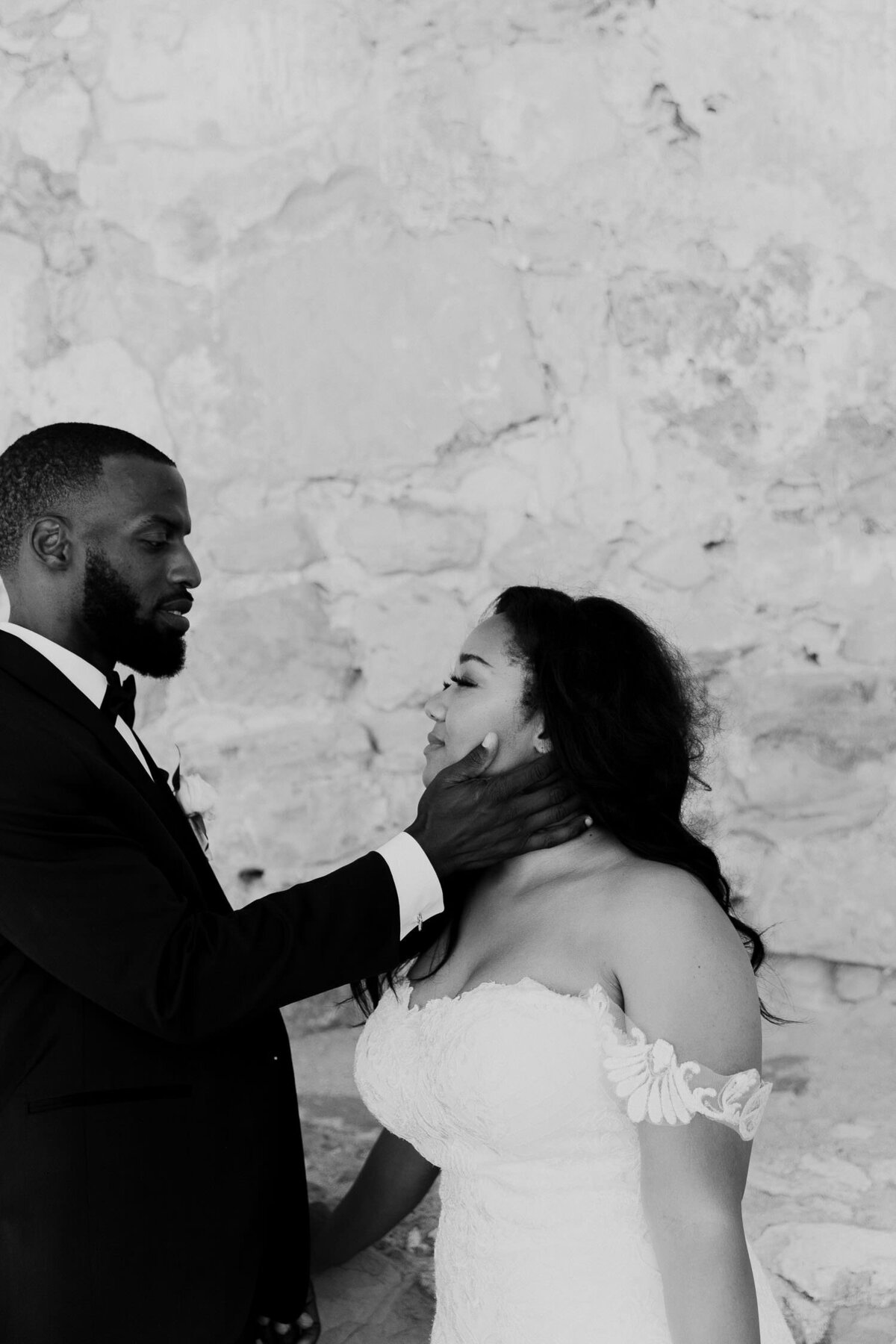 Groom is touching brides cheek during intimate moment at Mission San Juan Capistrano