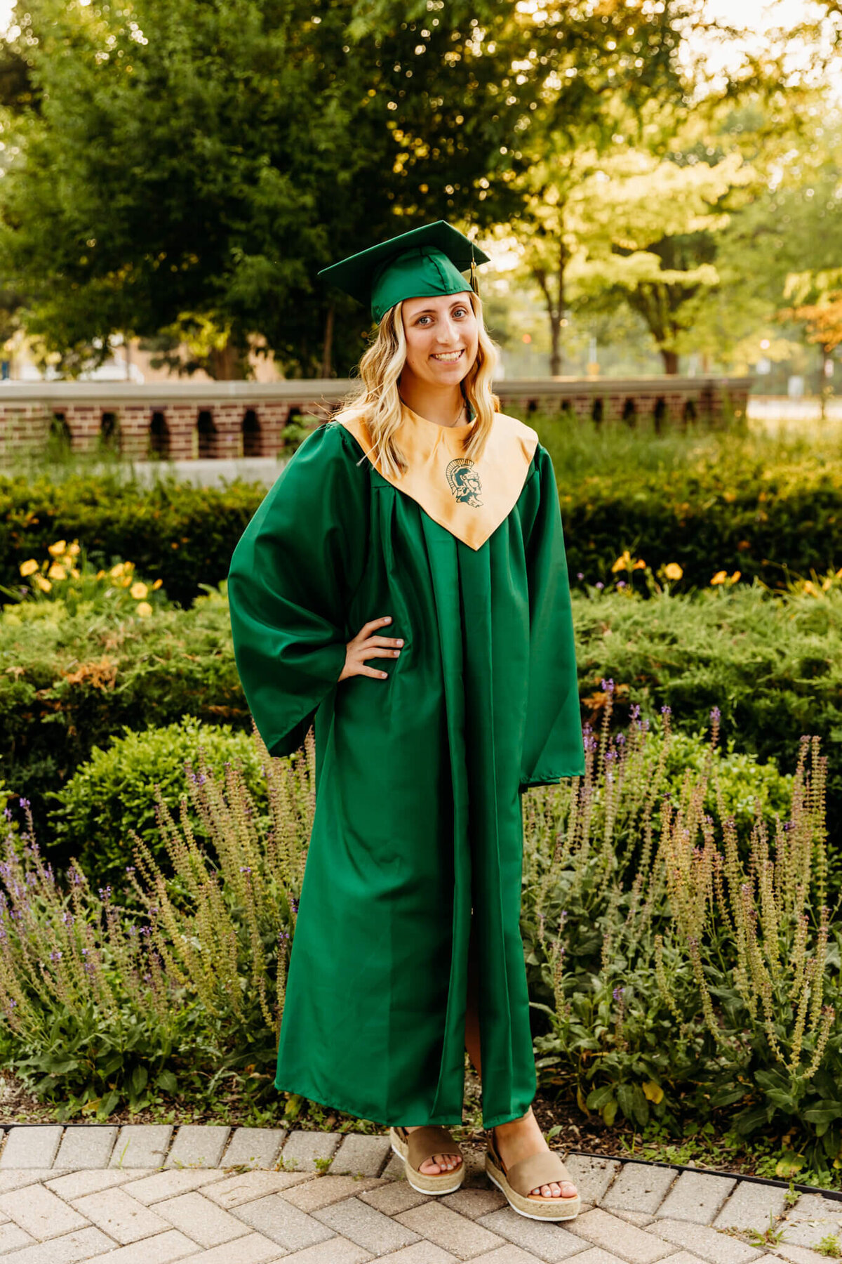 Beautiful young woman in a green cap and gown smiling while holding one hand on her hip at Oshkosh Public Museum