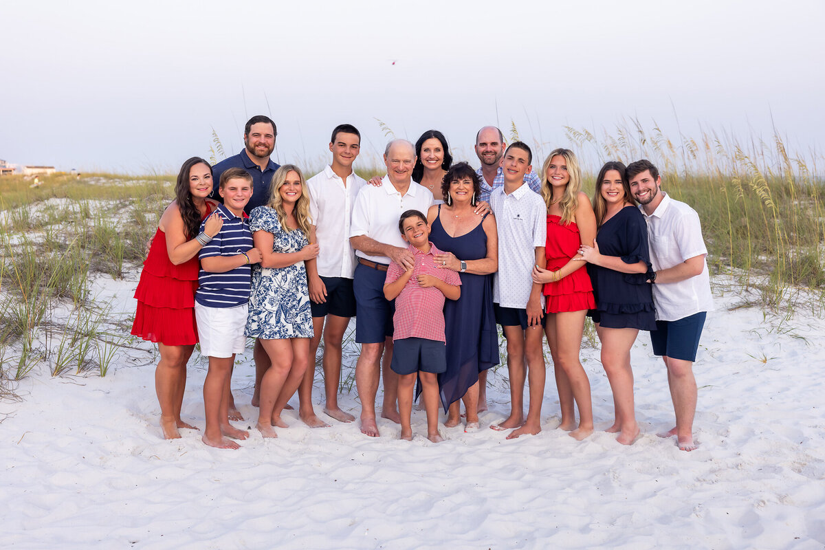 large multi-family portrait in destin, Florida.  They are wearing red, white and blue standing on white sand beach.