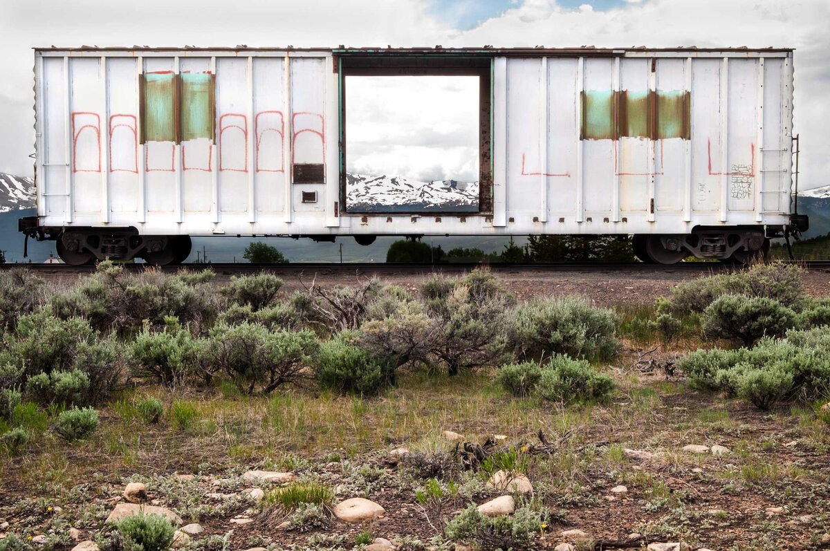 A train car with writing and the rockie mountains behind it