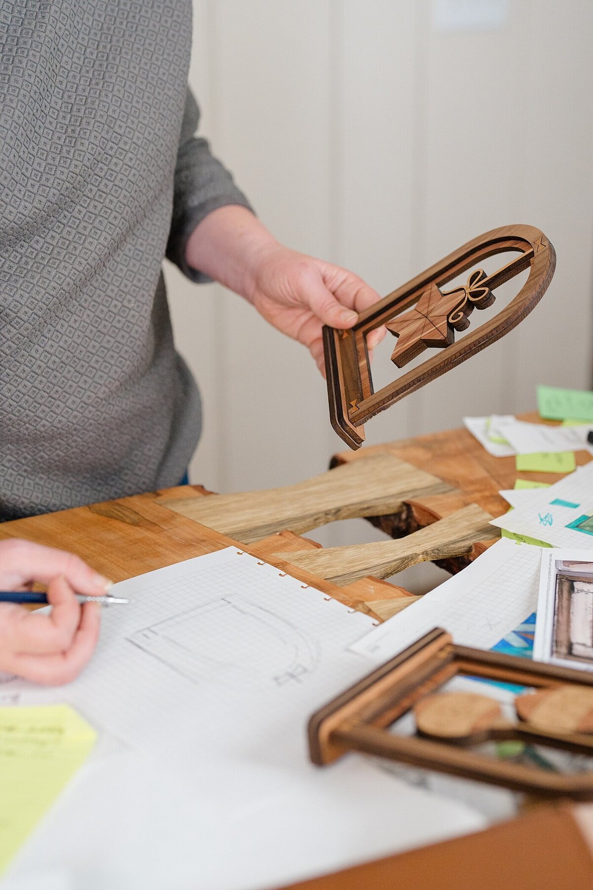 brand photographer captures behind the scenes photos of woman holding a wood worked piece and write notes about it for brand photos