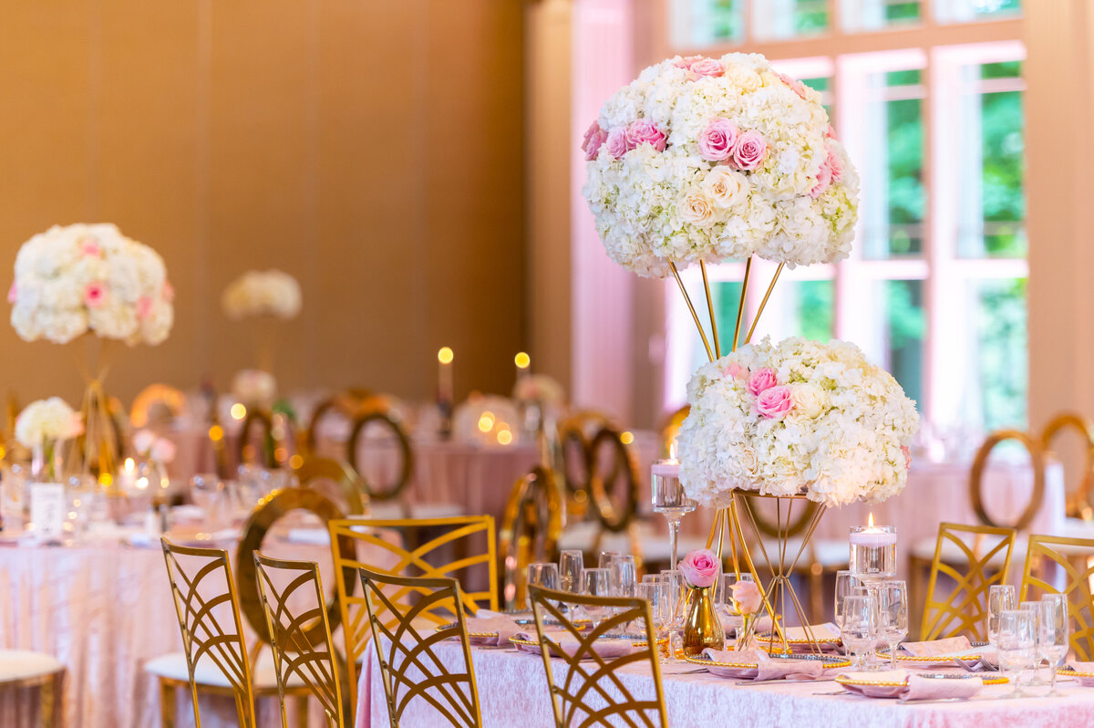 tables, chairs, and flower arrangements at a pink, white, and gold themed wedding reception