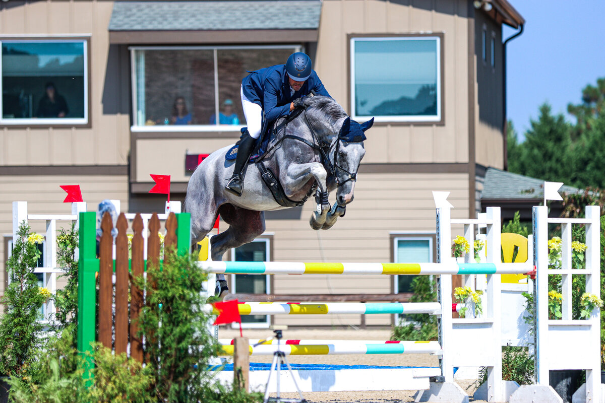 A grey horse jumping a large jump during an event at the Carolina Horse Park in Raeford, North Carolina.