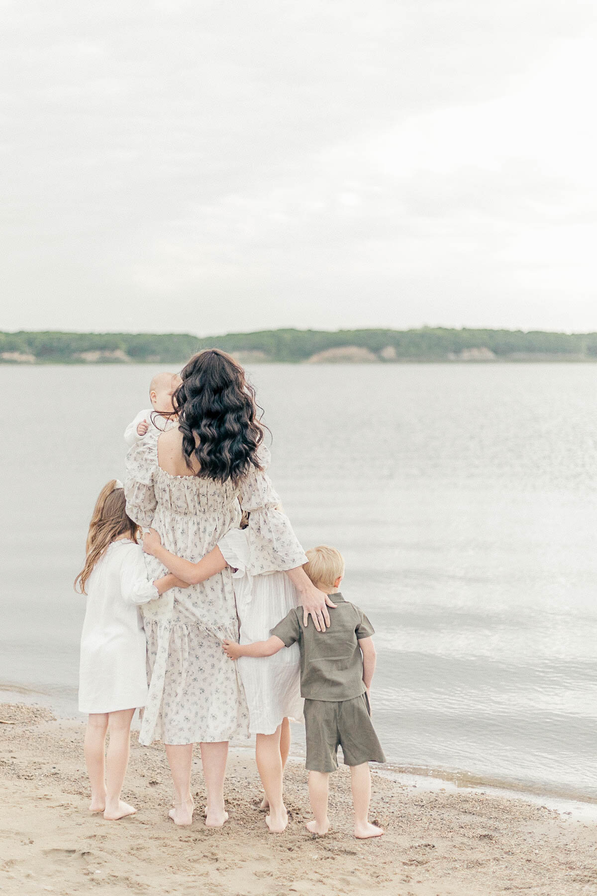 A mother with her four children standing side by side looking out over the water during their Kansas City family beach photography session.