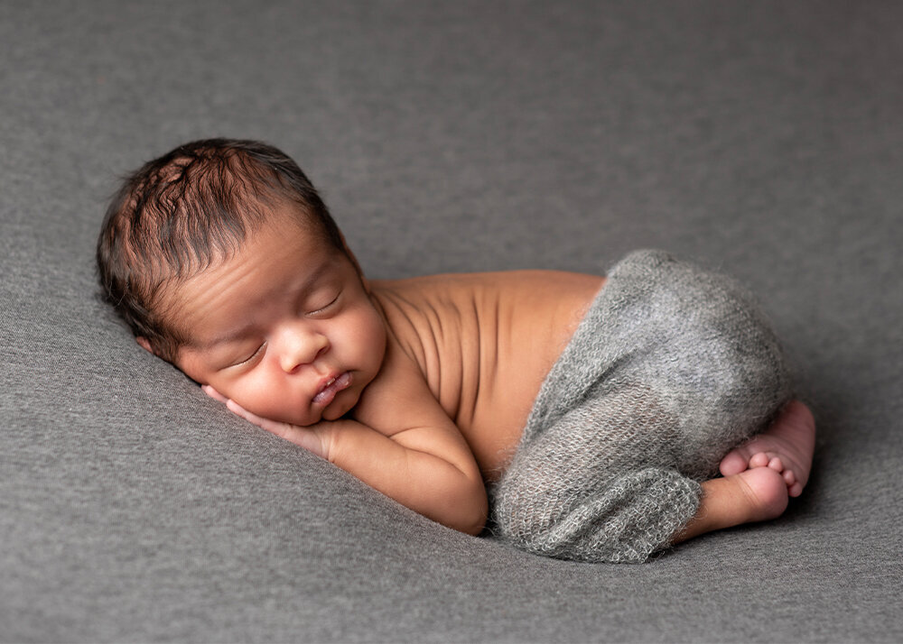 newborn-boy-in-grey-pants-on-grey-backdrop