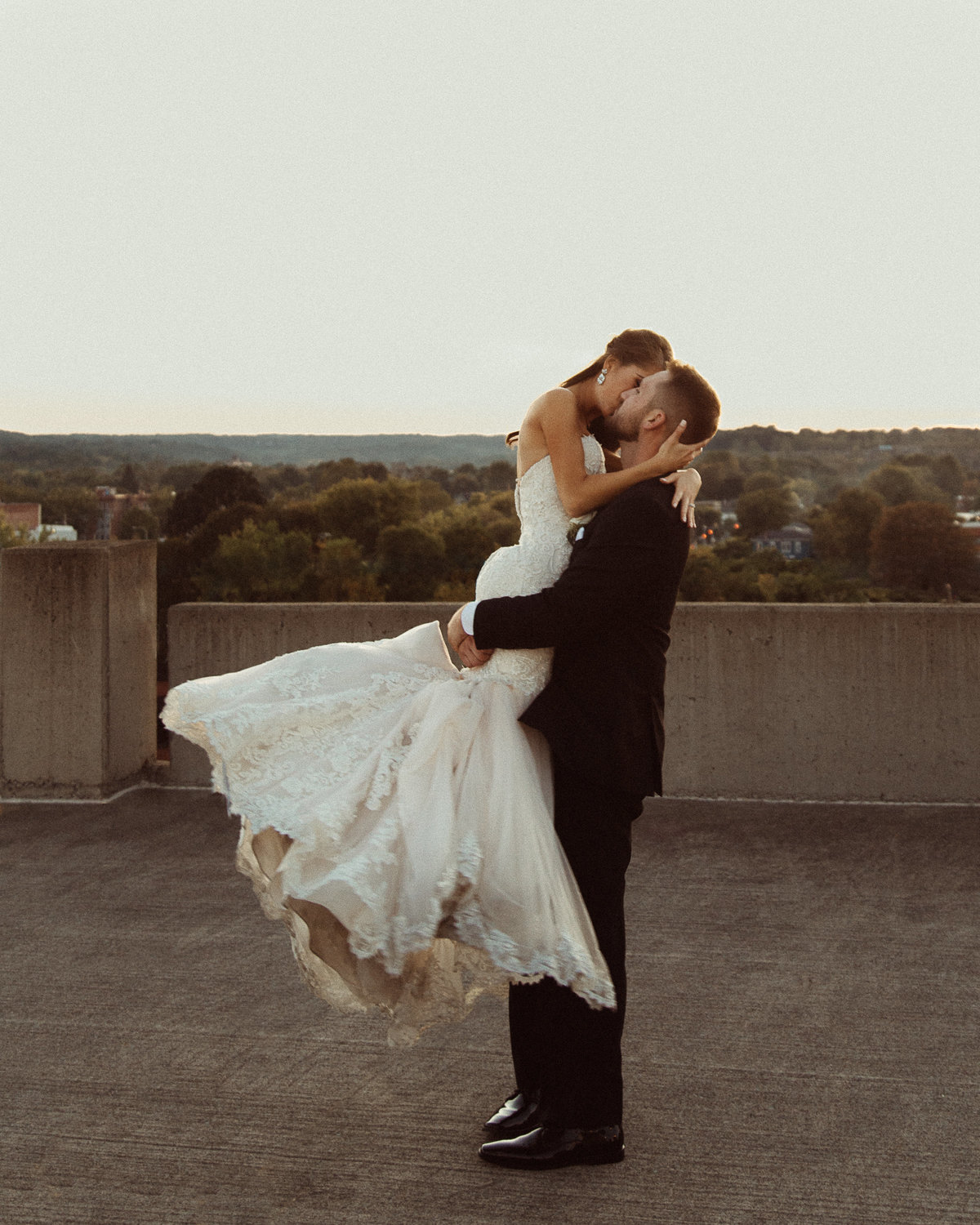 groom spins bride around on a rooftop with the city of Syracuse behind them