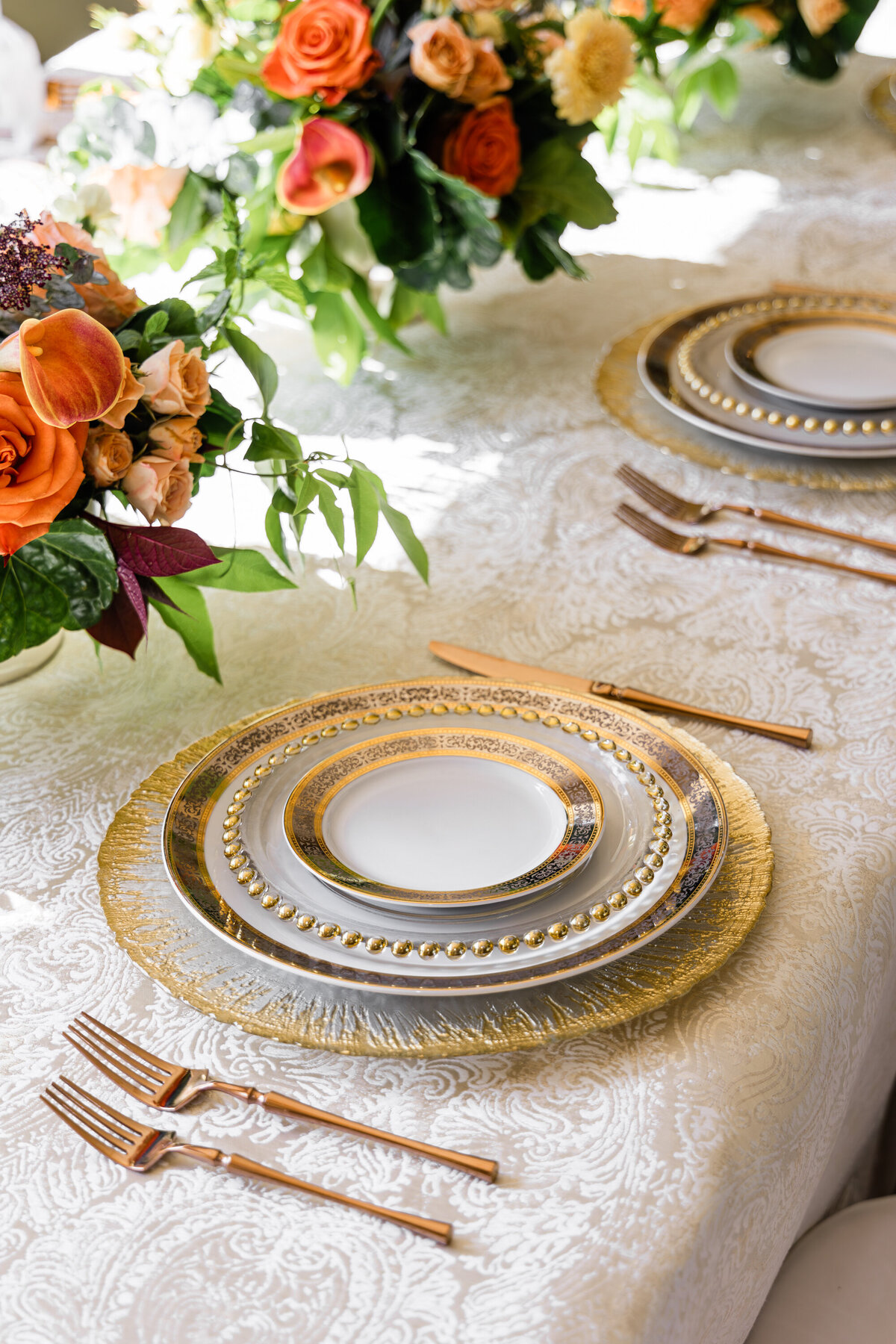 four plate mixed metals place setting with four piece rose gold flatware set and a orange rose and calla lily centerpiece