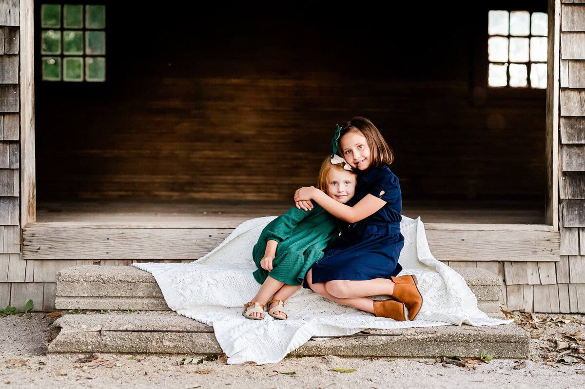 Sisters hugging during family session at old boat house located at Fabyan Forest Preserve in Geneva, IL.