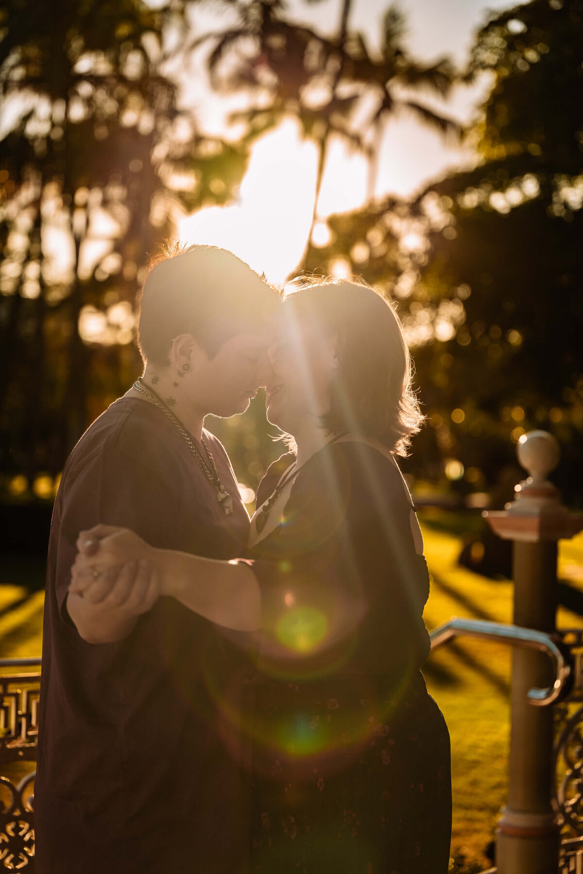 A couple shares a romantic kiss against a vibrant sunset, with the sun casting a warm glow around them. - photo by Jamie Simmons