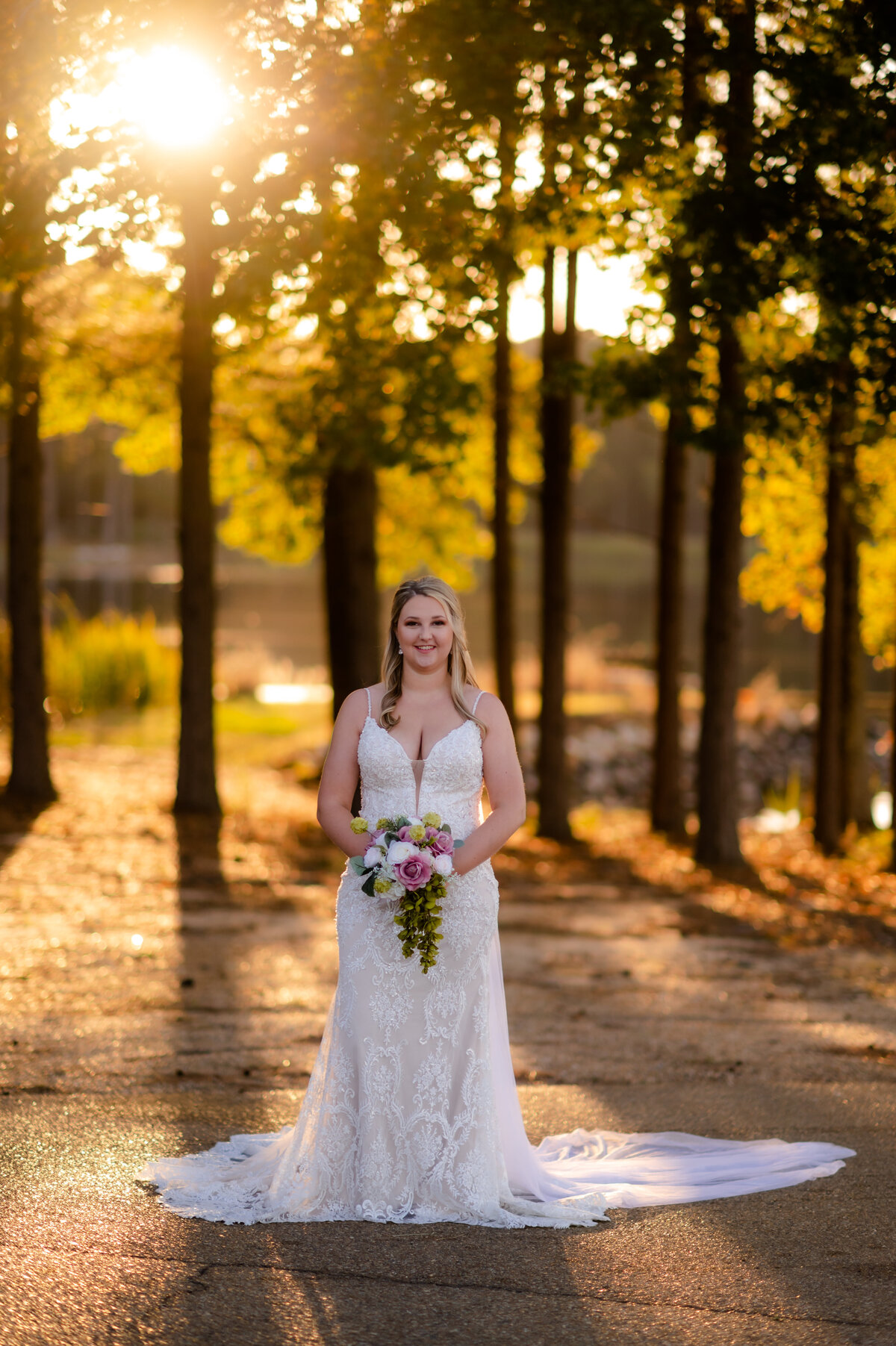woodland wedding in the fall with bride holding a small floral bouquet in front of her while smiling at the camera with the golden sun setting behind her