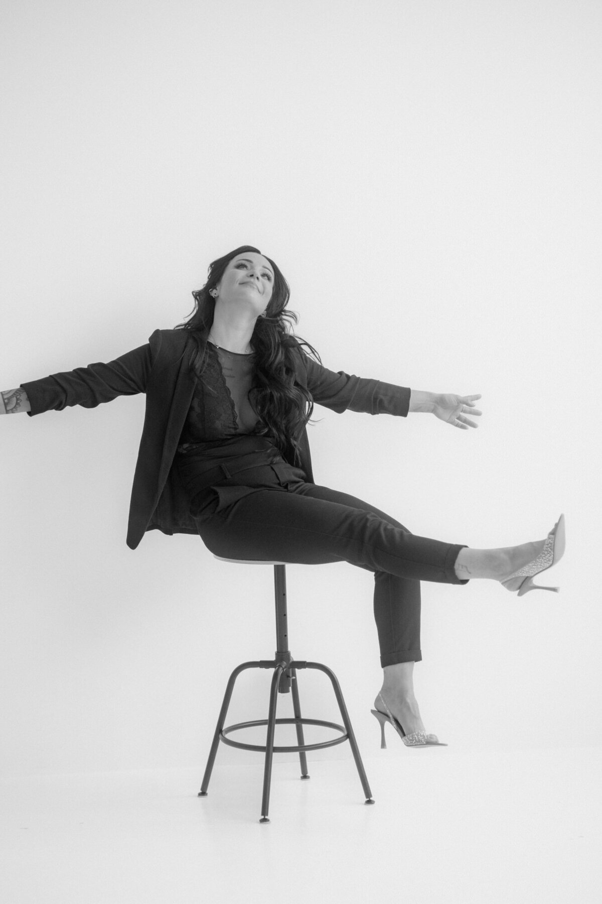 A business woman sits on a stool stretching her arms wide, while looking up.