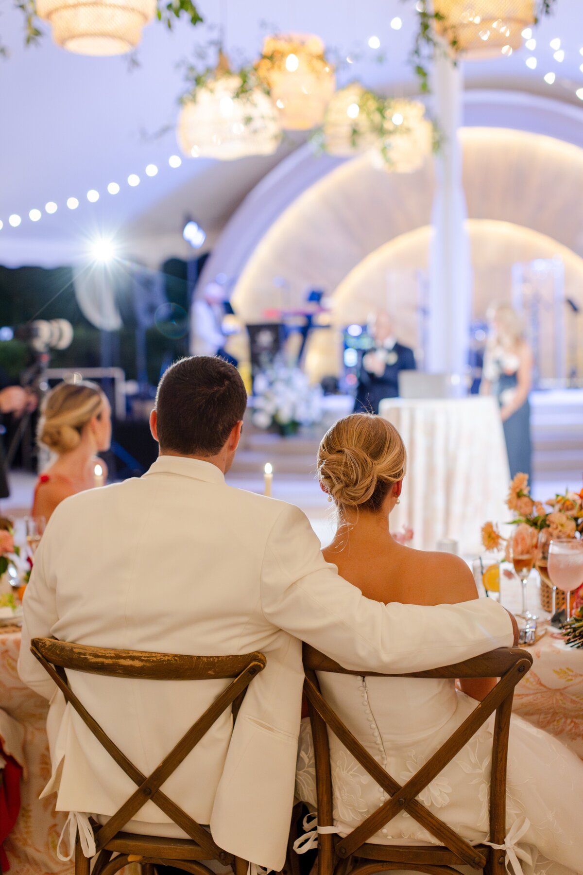 groom with arm around bride during speeches at sweetheart table