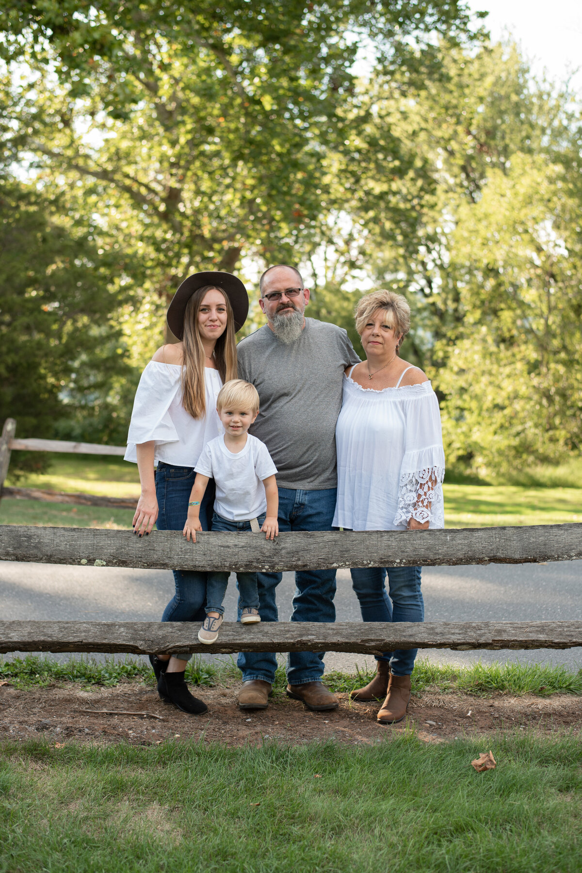 Family of four posed behind a wooden fence with trees behind them.