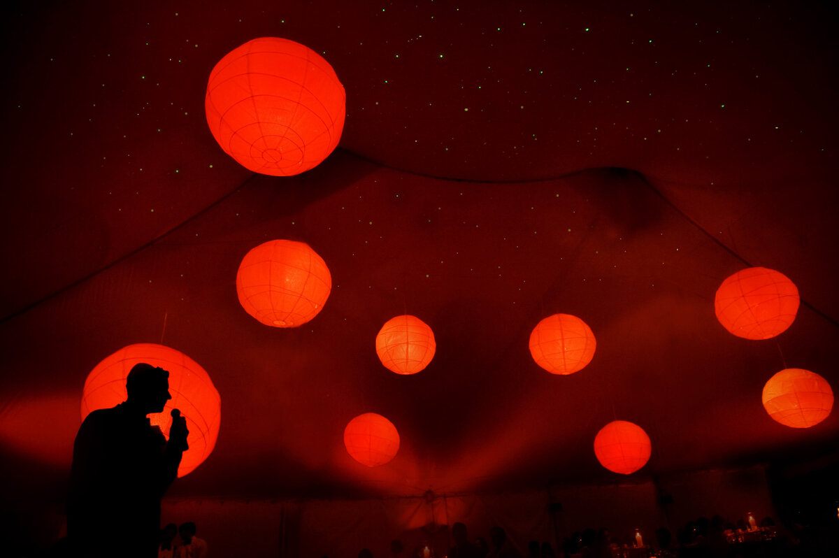 Red circular lights hanging from a tent during a wedding reception.