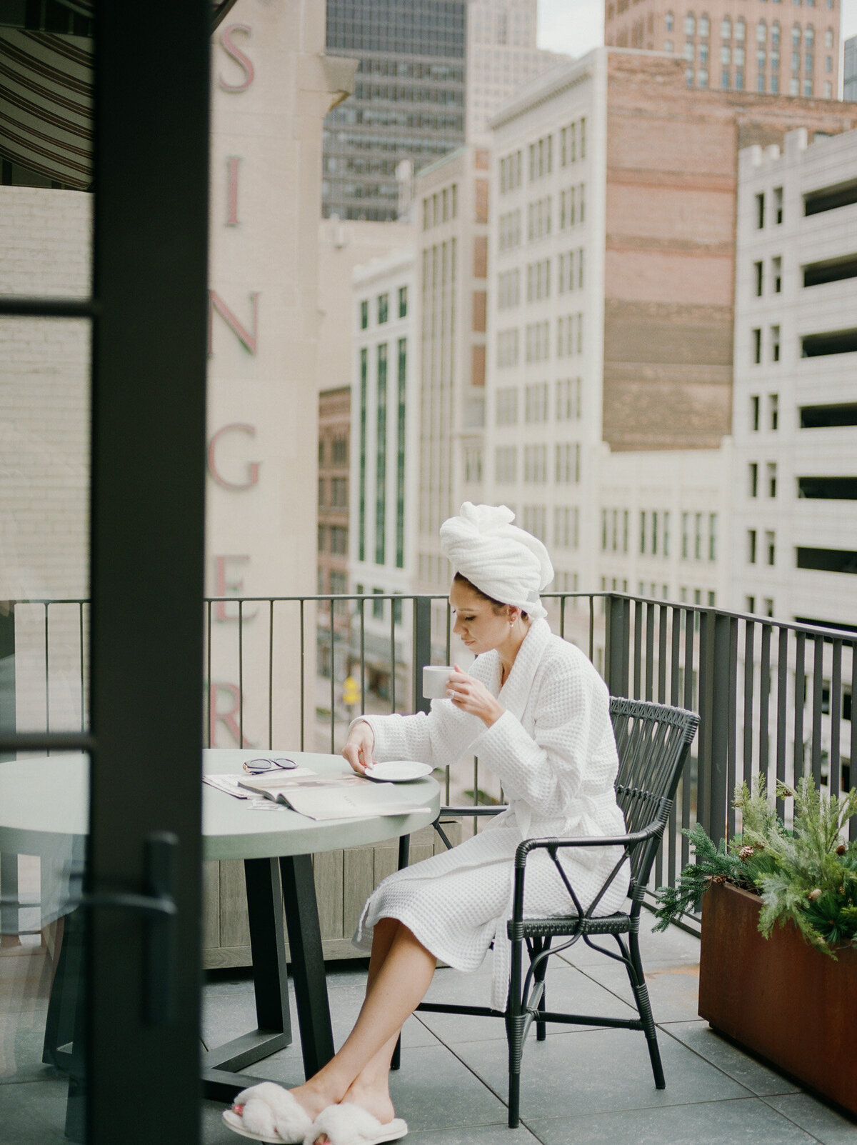 woman in bathrobe and hair towel reads magazine on hotel balcony in Detroit