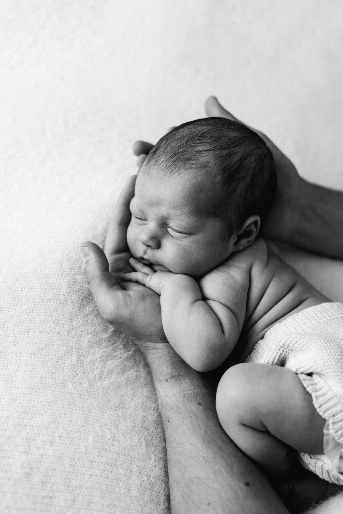 a newborn baby sleeping in fathers hands in west sussex newborn photoshoot