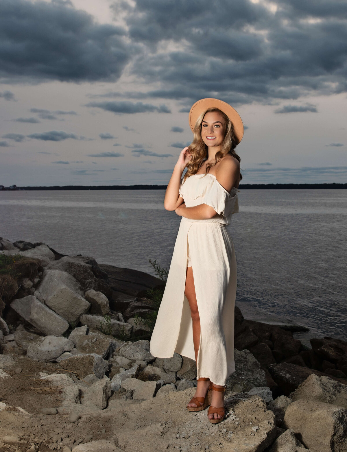 Photo of a senior standing on a rock in a white dress and hate on the Erie Pa waterfront