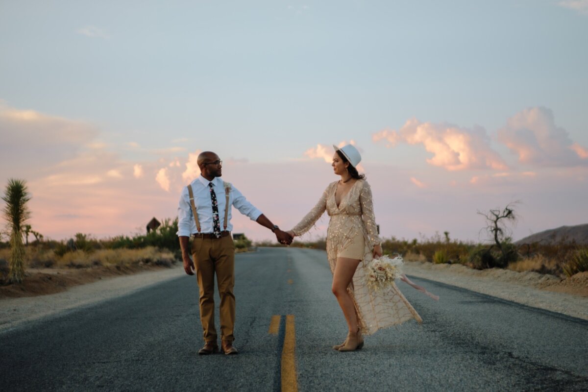 A bride and groom stand in the road during sunset in Joshua Tree National park