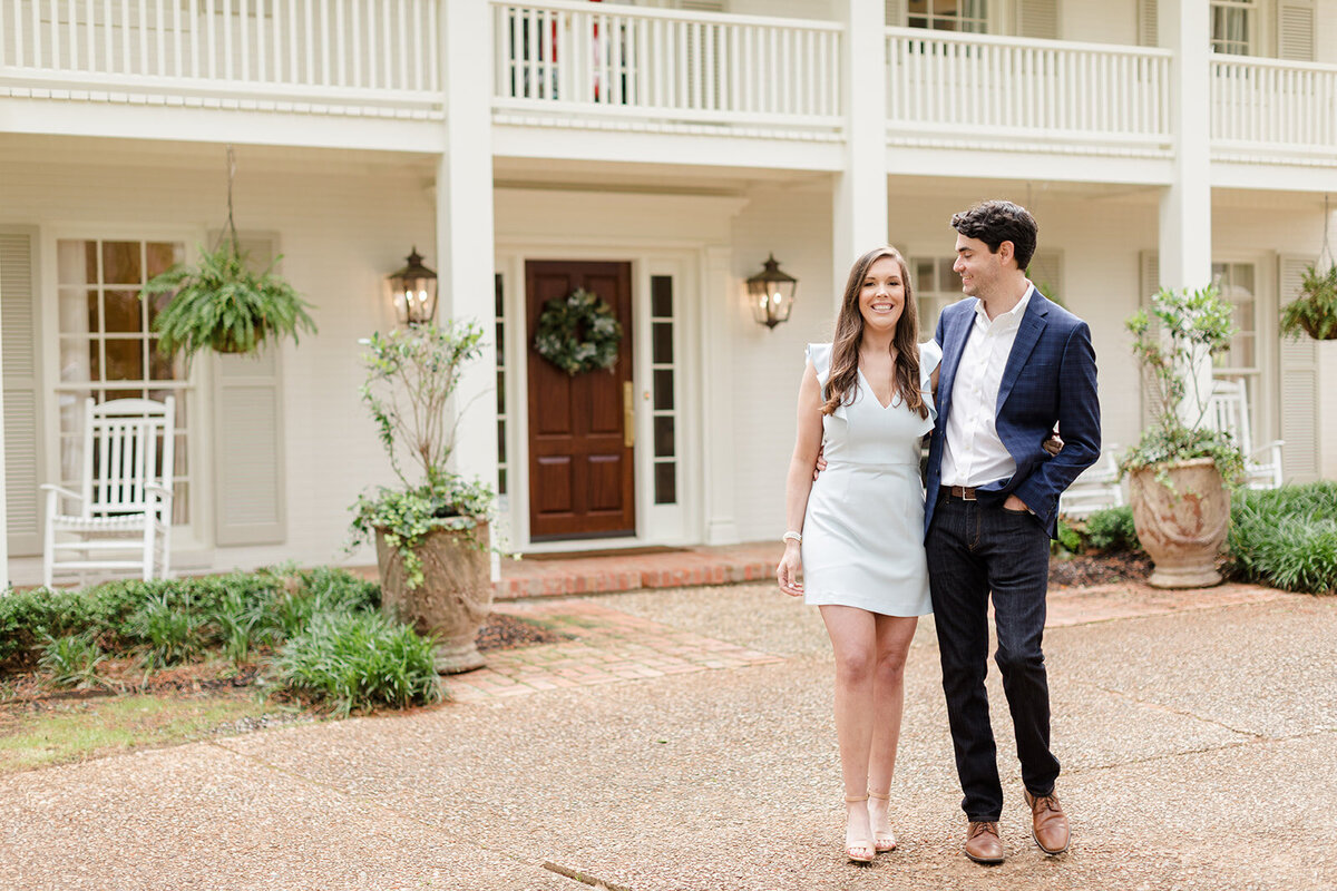 Engagement photo of couple walking in front of house