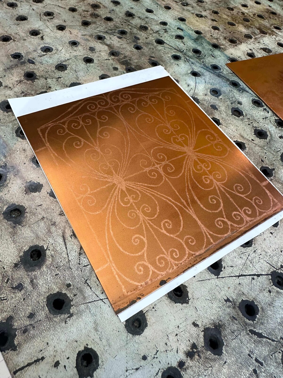 A copper plate with rosin aquatint texture and delicate linework resting on a perforated metal surface.