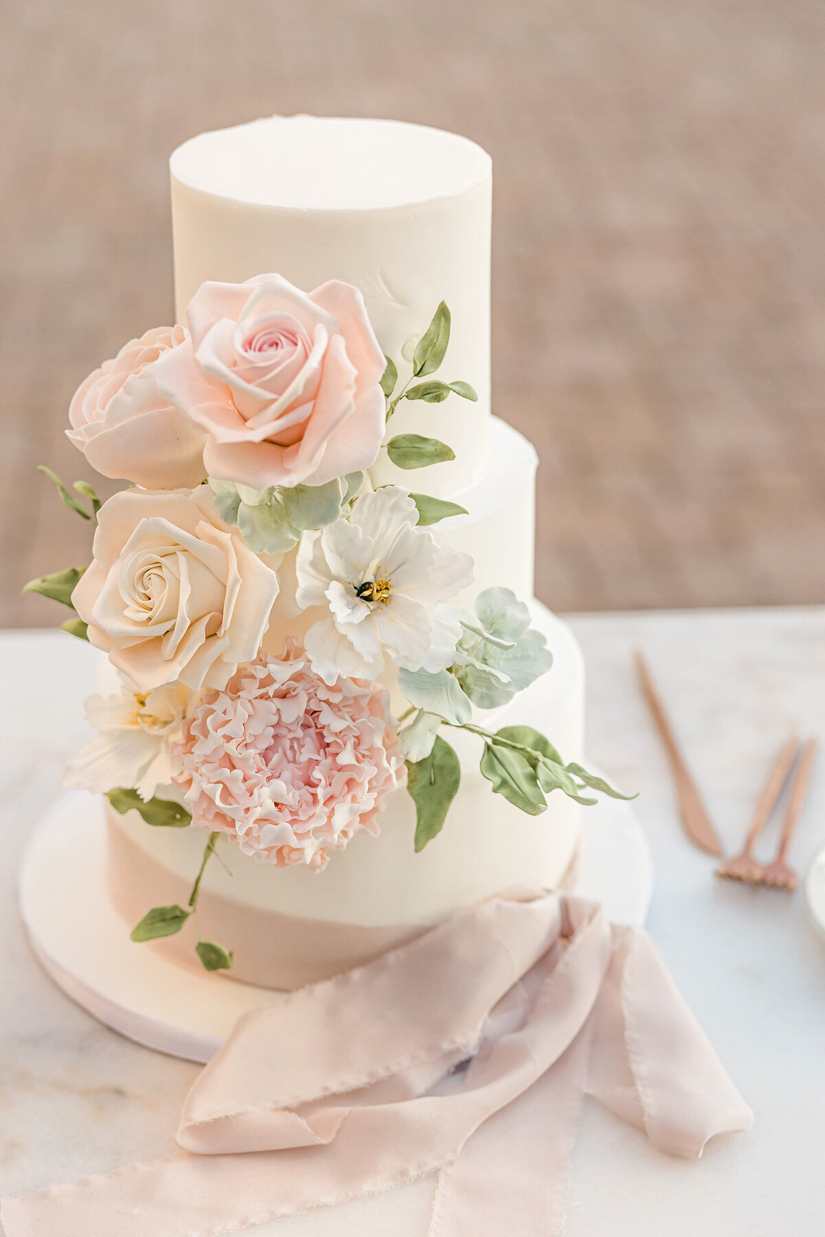 White cake on a table with pink and ivory florals. 
