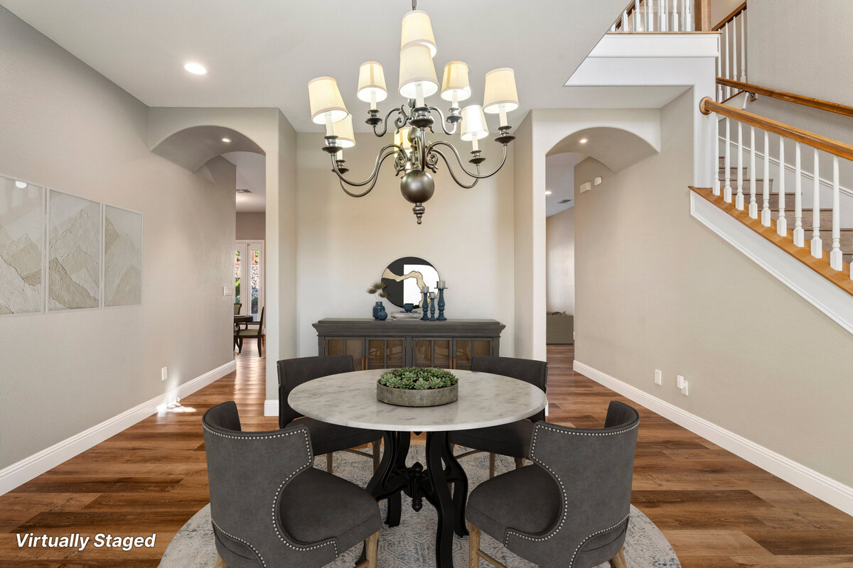 Virtually staged dining room with round table and grey chairs. Arched passways on either side of the room and a staircase to the right.