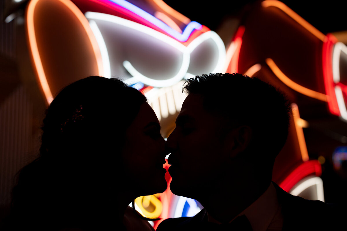 A couple kissing backlit by a neon sign