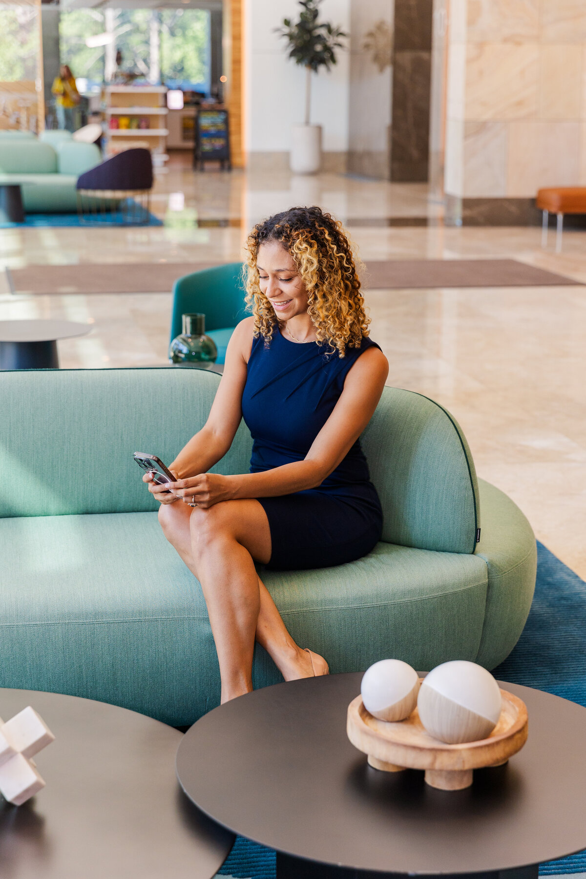 woman in business outfit sitting in an office lobby checking her phone