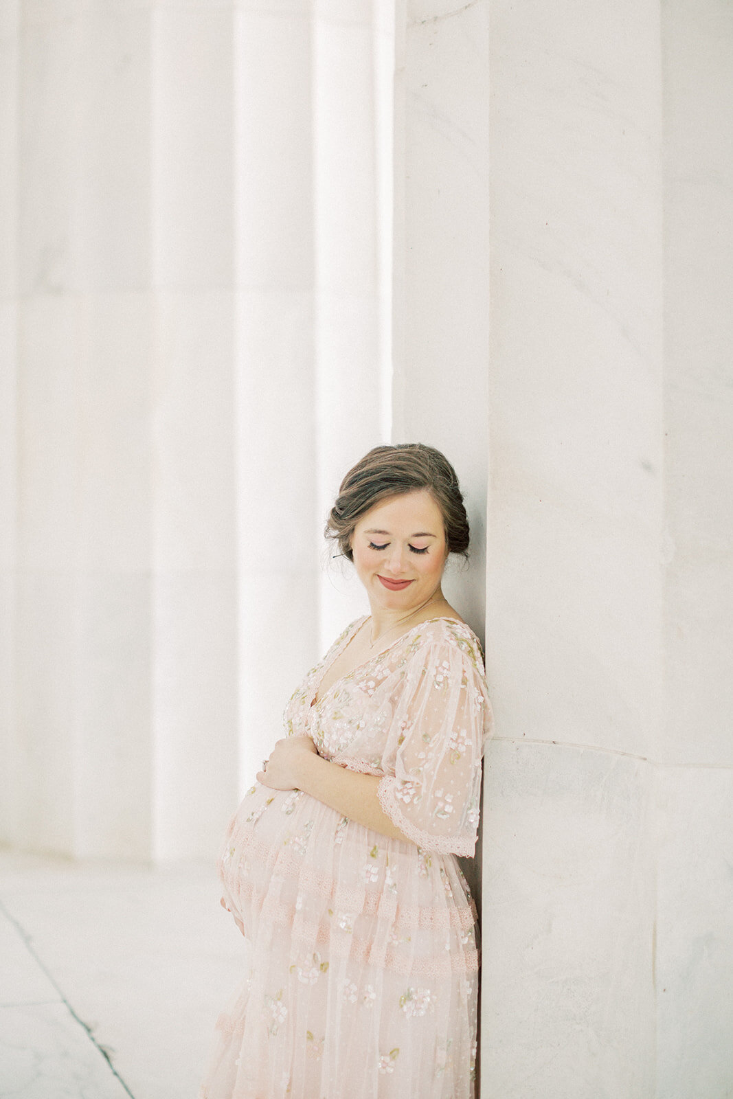 Pregnant mother in Needle & Thread rose sequin dress leans up against pillar at Lincoln Memorial.