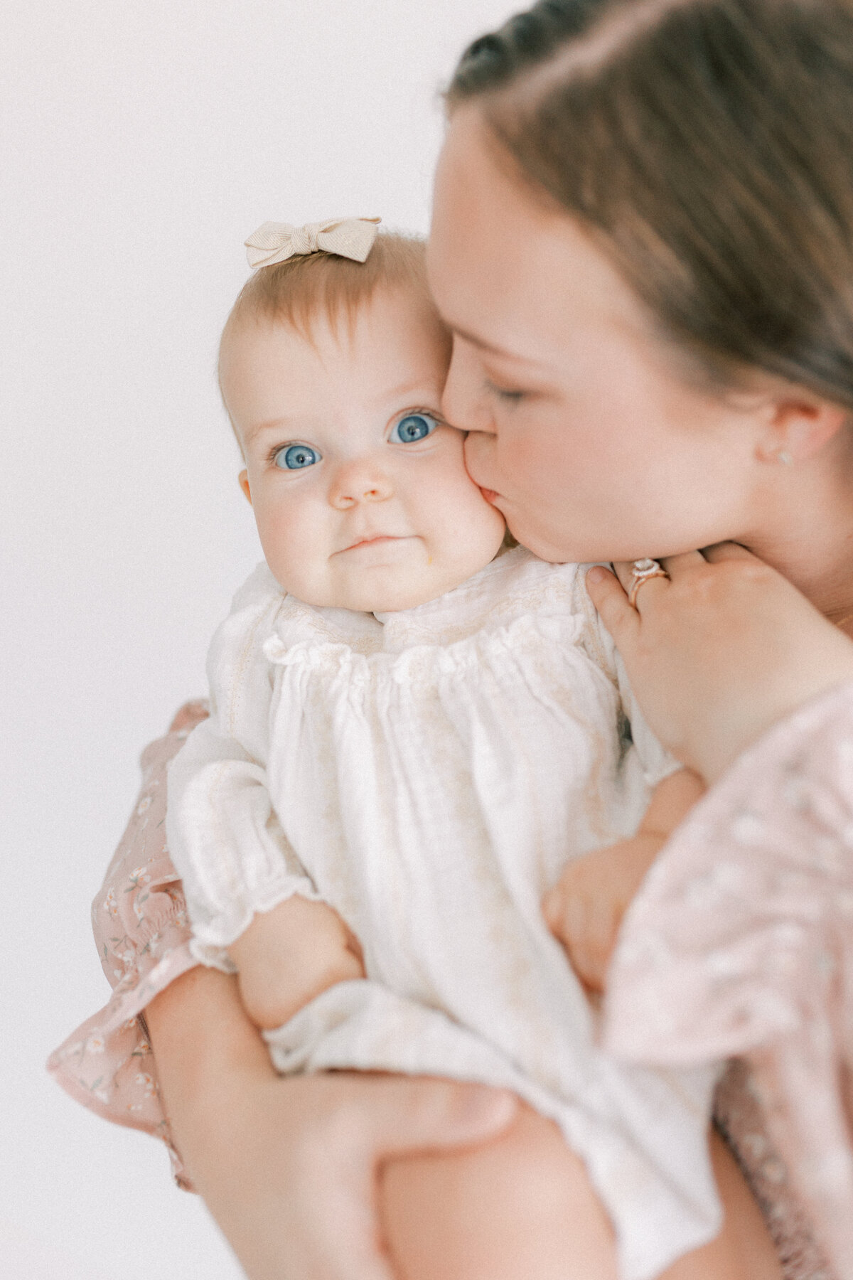 mom in pink dress kissing little girls cheek in cream dress