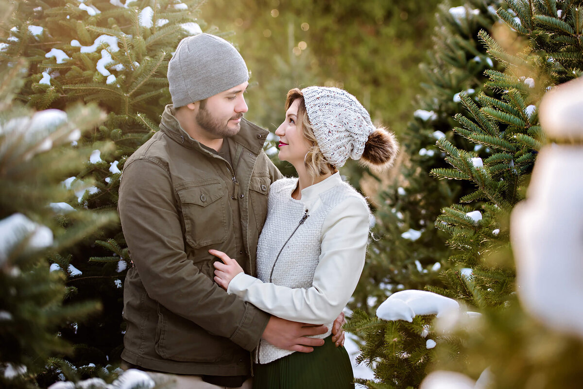 husband and wife hugging at a Christmas tree farm with snow for their Christmas Family Photography Session