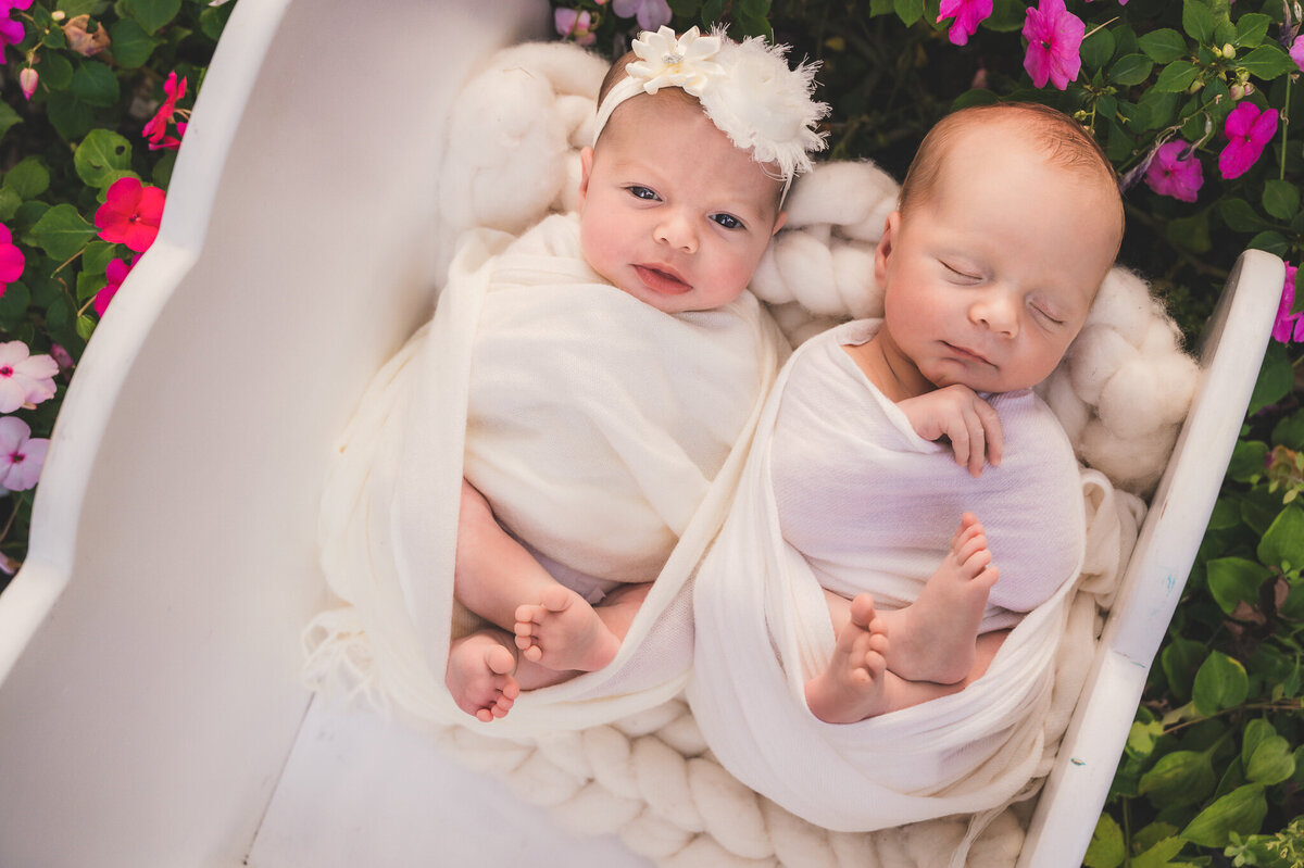 Boy and girl newborn twins at their newborn session in Greater Toronto Newborn photos wrapped in white on a white bed surrounded by flowers.