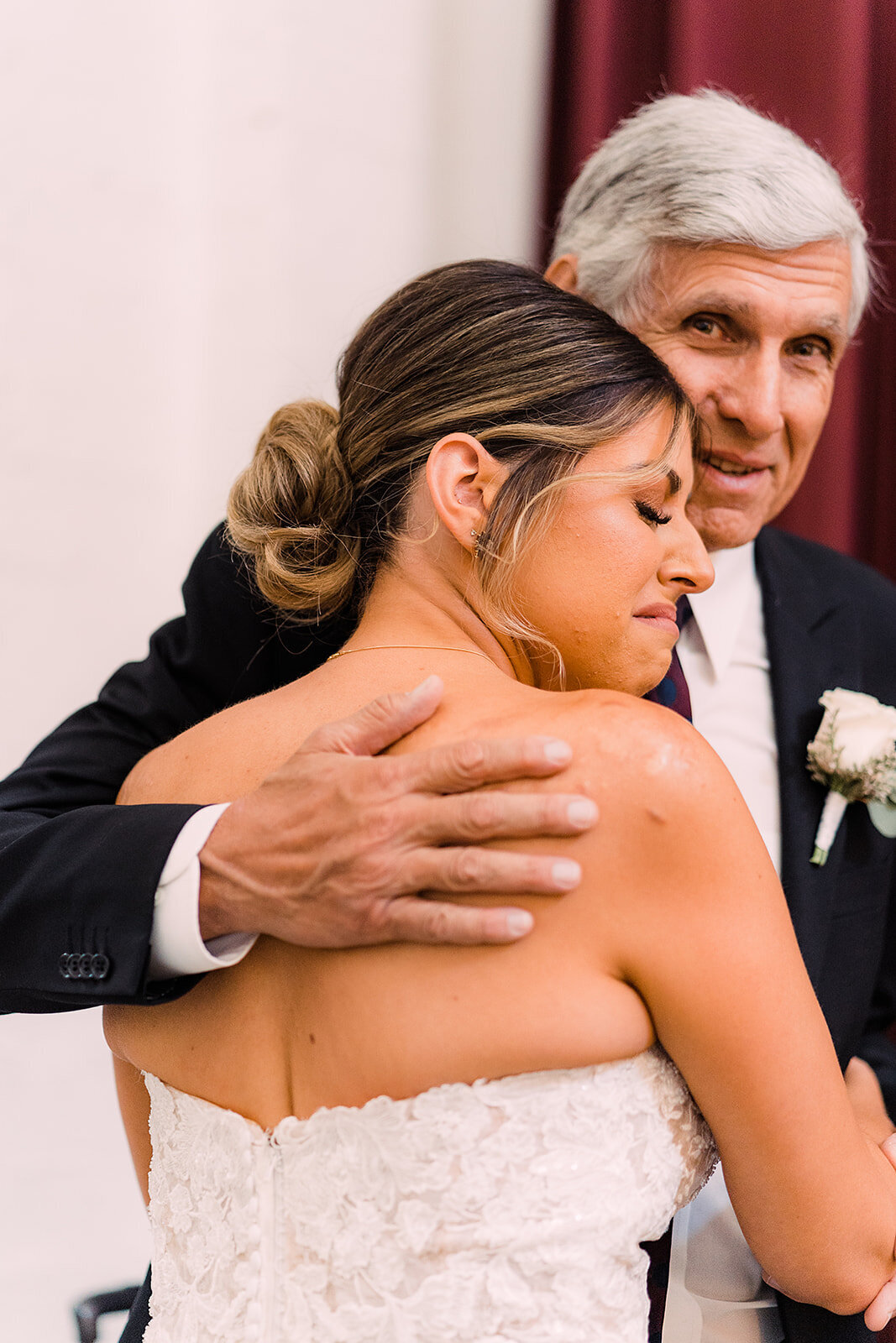 Bride, with an emotional expression, embraces her father in a heartfelt hug on her wedding day.