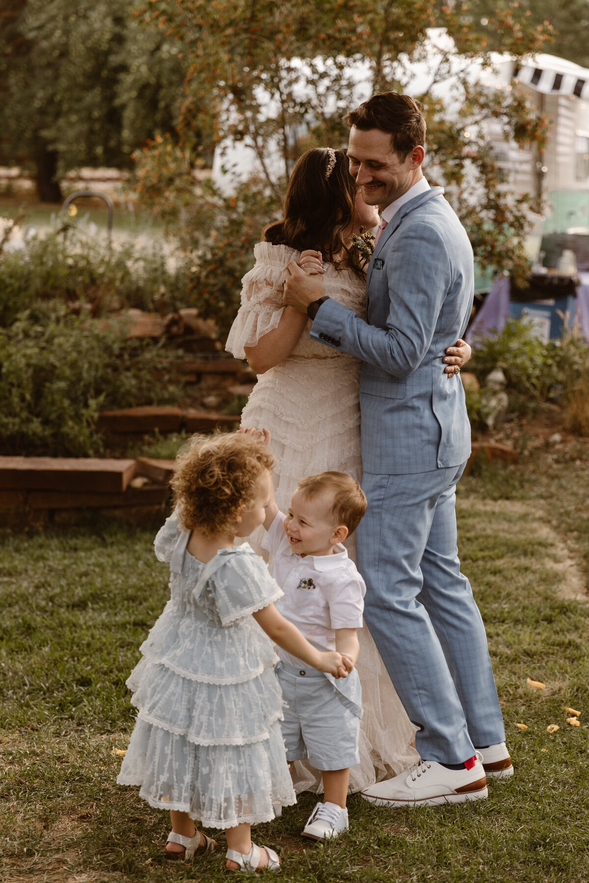 Bride and groom share a joyful first dance with their young children at an outdoor Colorado wedding, surrounded by greenery and rustic charm.