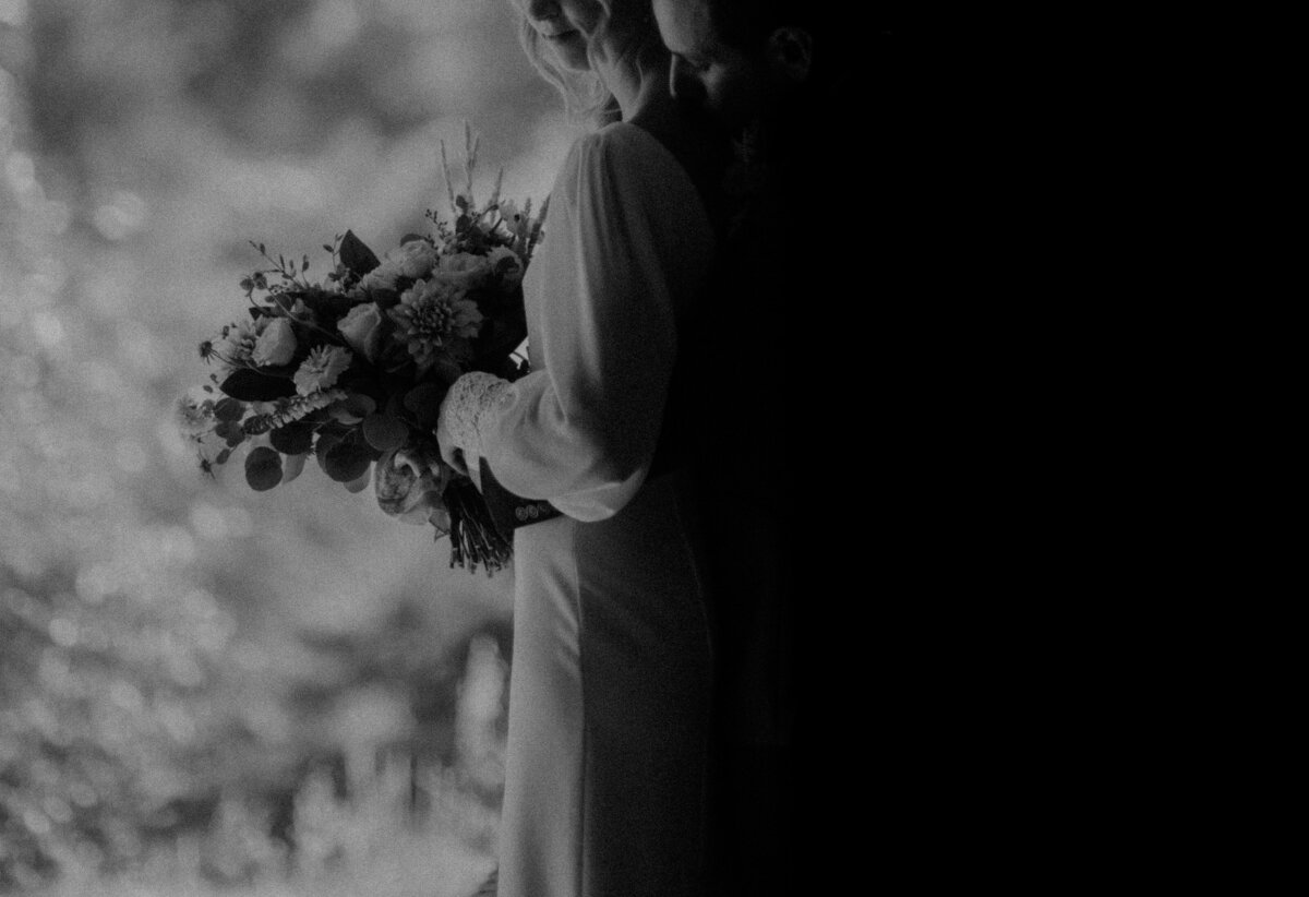 Groom holding the bride from behind with the camera focusing on the bouquet in the brides hands