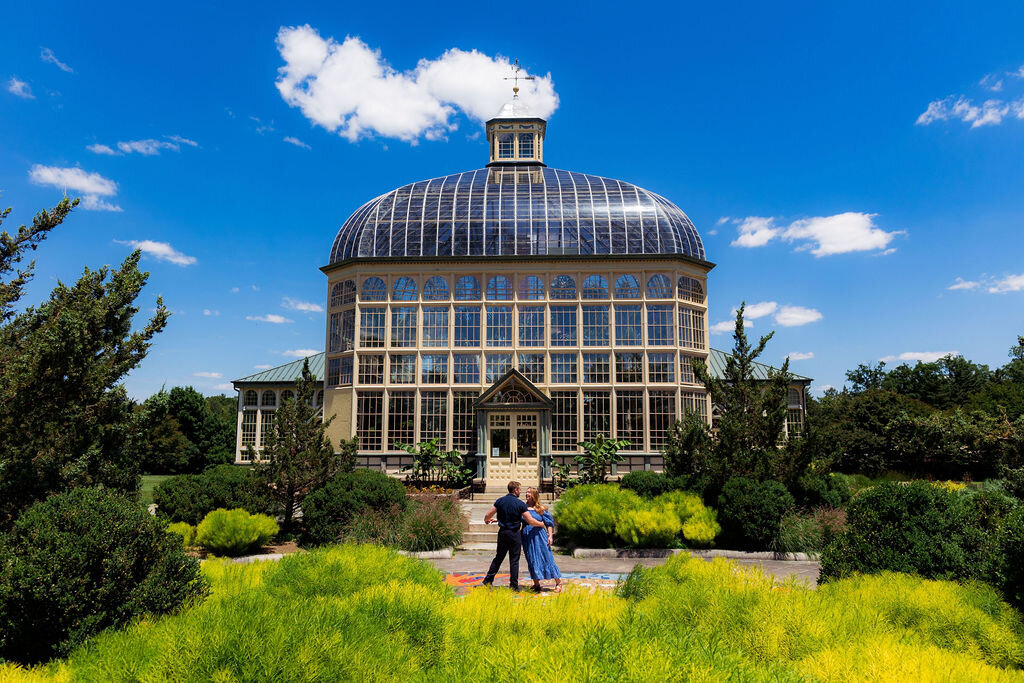 Two people with their arms around each other in front of a conservatory