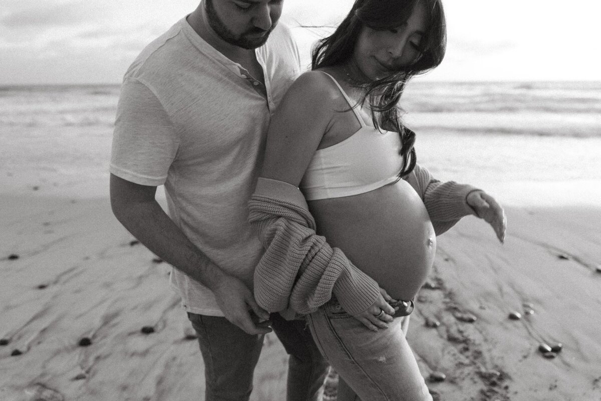couple poses on beach for family maternity session in san diego