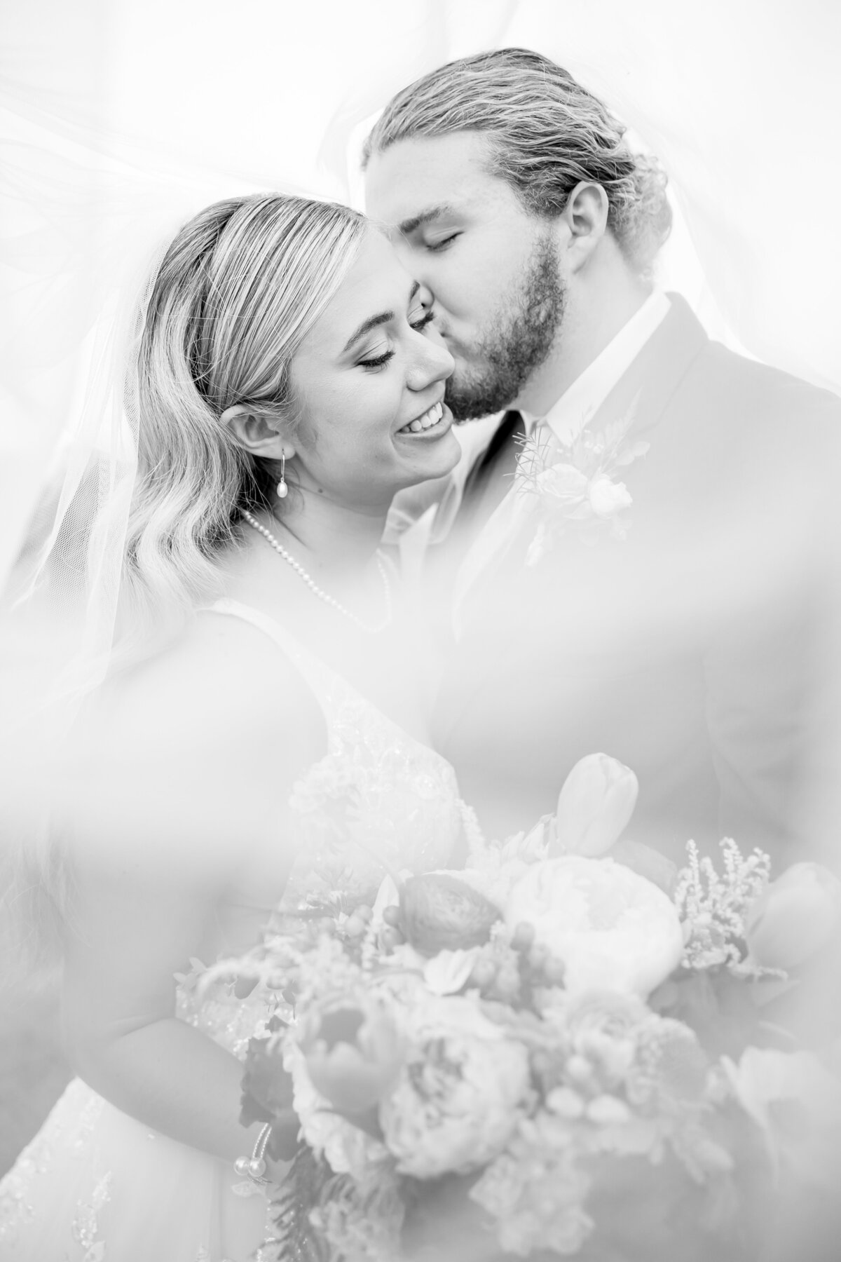 black and white photo of groom kissing bride on the cheek