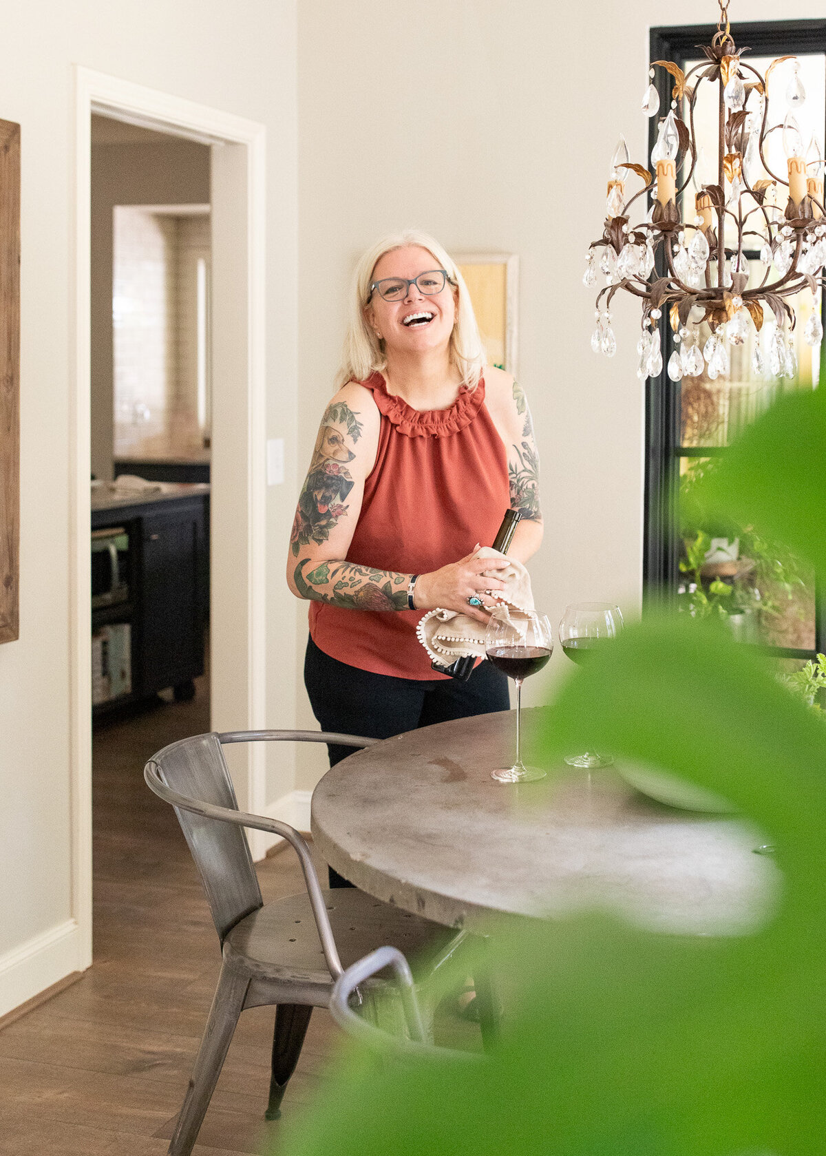 Woman laughing in dining area in a farmhouse as she opens a bottle of red wine. 