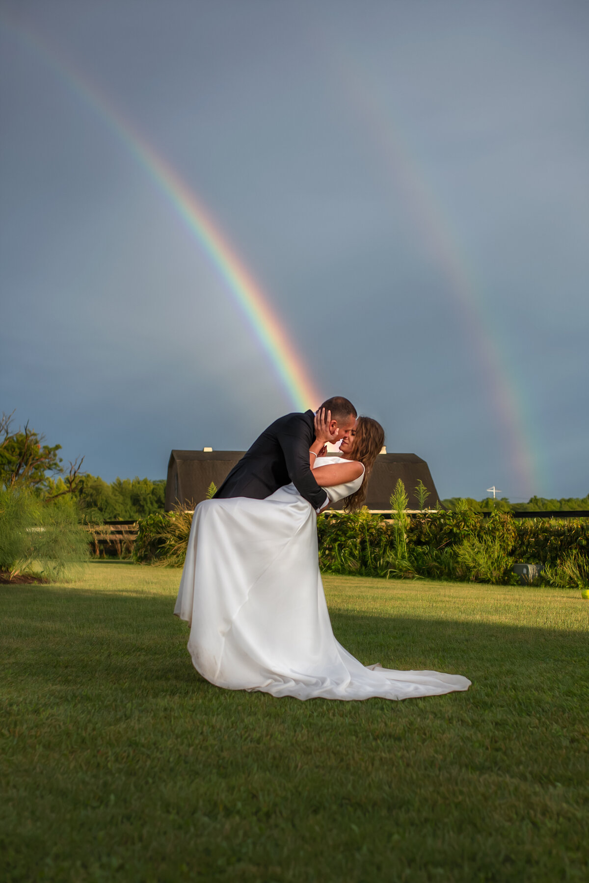 groom dips the bride for a kiss after the rain when two rainbows show up in the sky