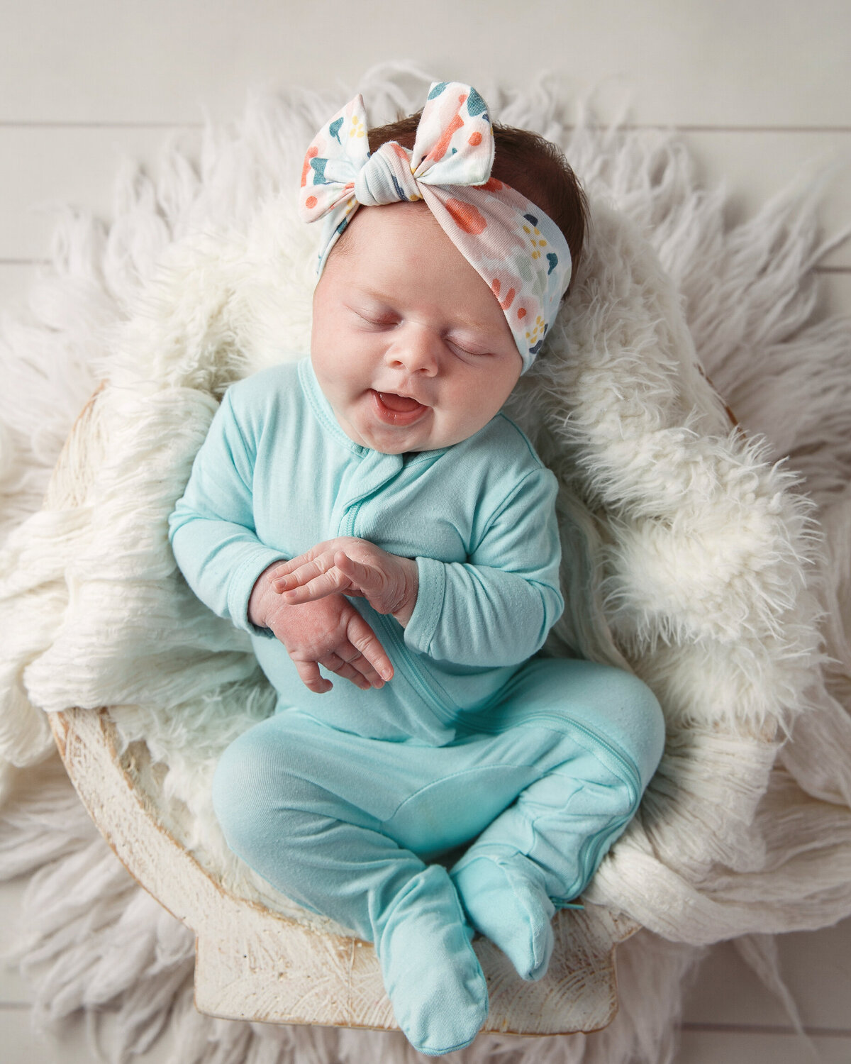 Cute photo of a smiling infant wearing a blue sleeper and a flowered headband