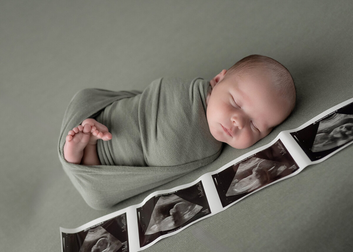 A newborn baby sleeps next to its sonogram in a studio
