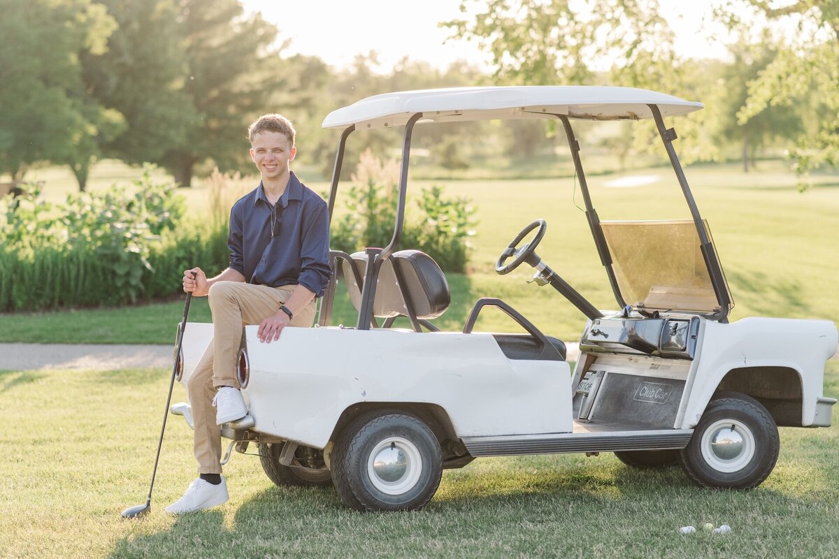 a guy sitting on the back of a golf cart while holding a club