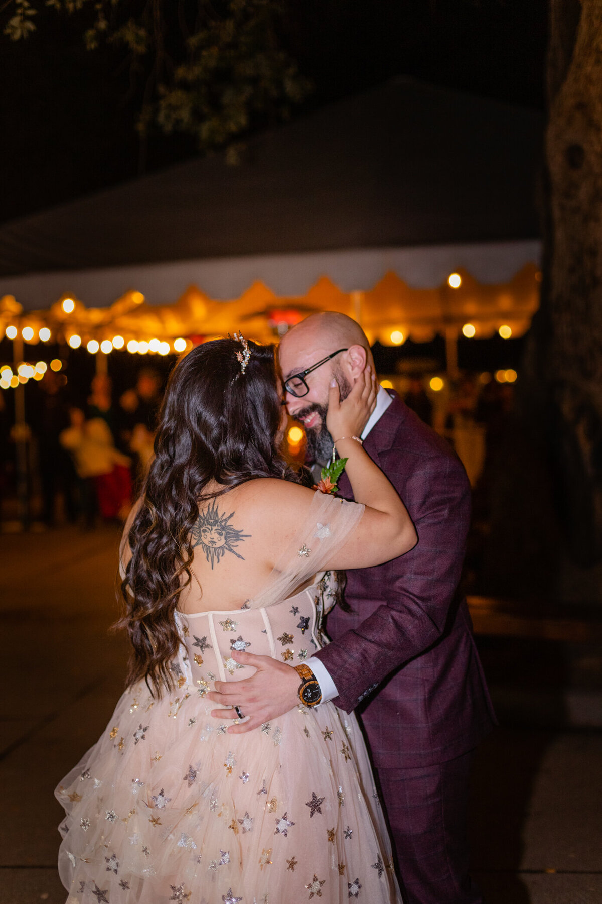 bride and groom smile in front of fairy lights