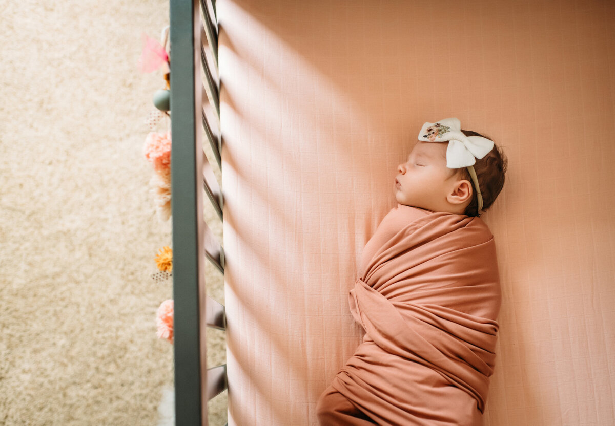 Newborn Photographer, Swaddled baby girl in a pink swaddle inside of a crib sleeping.