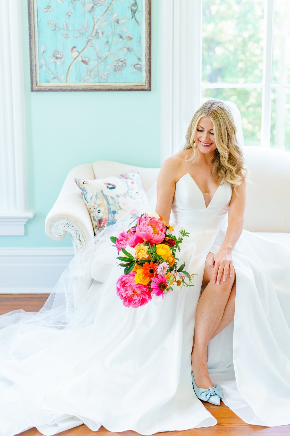 A bride sits on an elegant couch in a bridal suite at her Raleigh wedding.