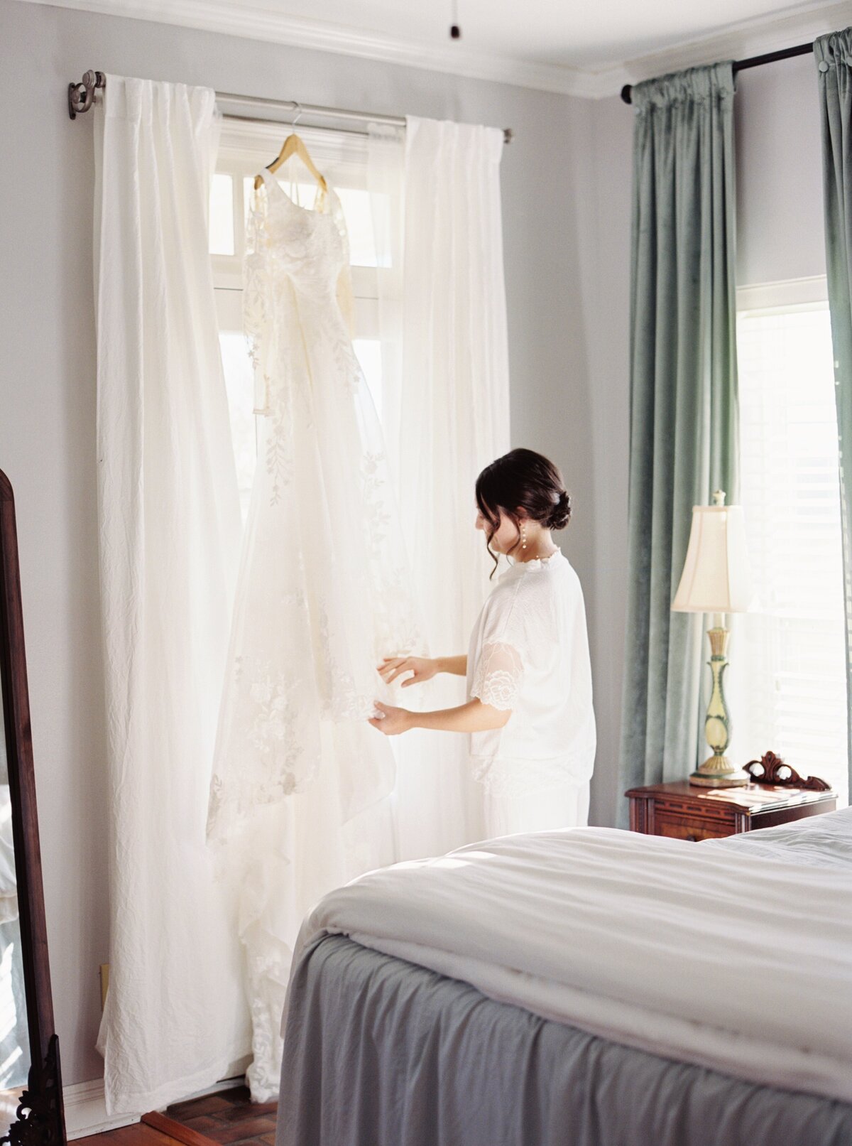 Bride admiring her wedding gown as she stands beside it on her wedding day, captured on film by Morgan Alysse, Louisiana film photographer.