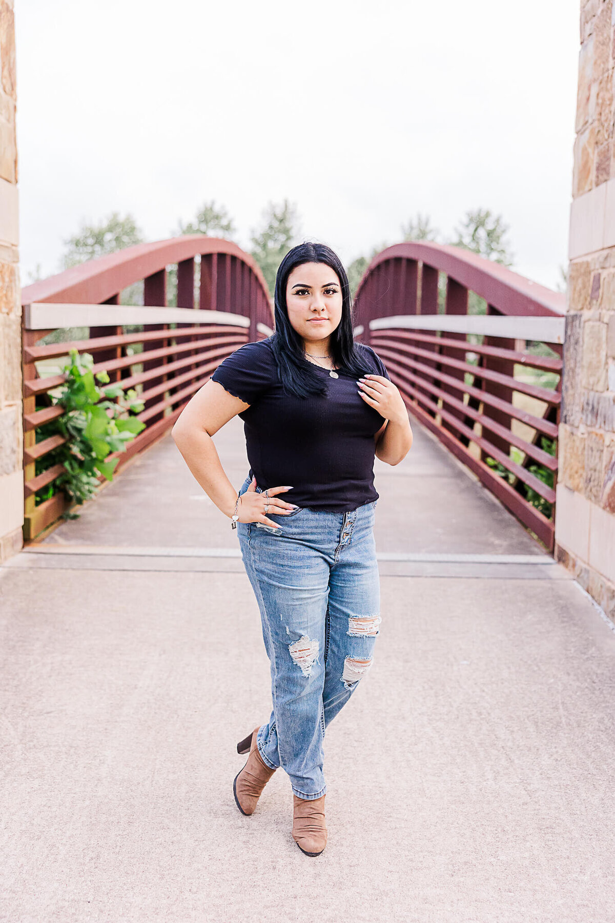 Lady wearing jeans and black top touching her hair on bridge in Cross Creek Ranch
