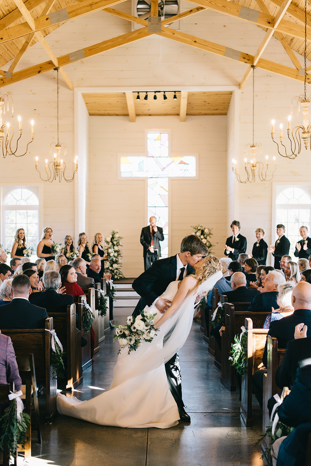Bride and groom kissing in aisle at wedding ceremony with white and green floral arrangements designed by Abby Grace Florals at Saluda SC wedding