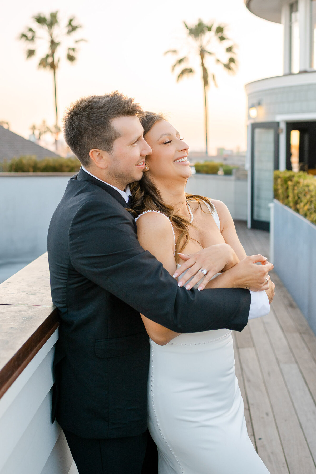 The newlyweds embrace on the Topside Roof Deck of Lido House in Newport Beach, with the golden sunset and palm trees framing a romantic moment